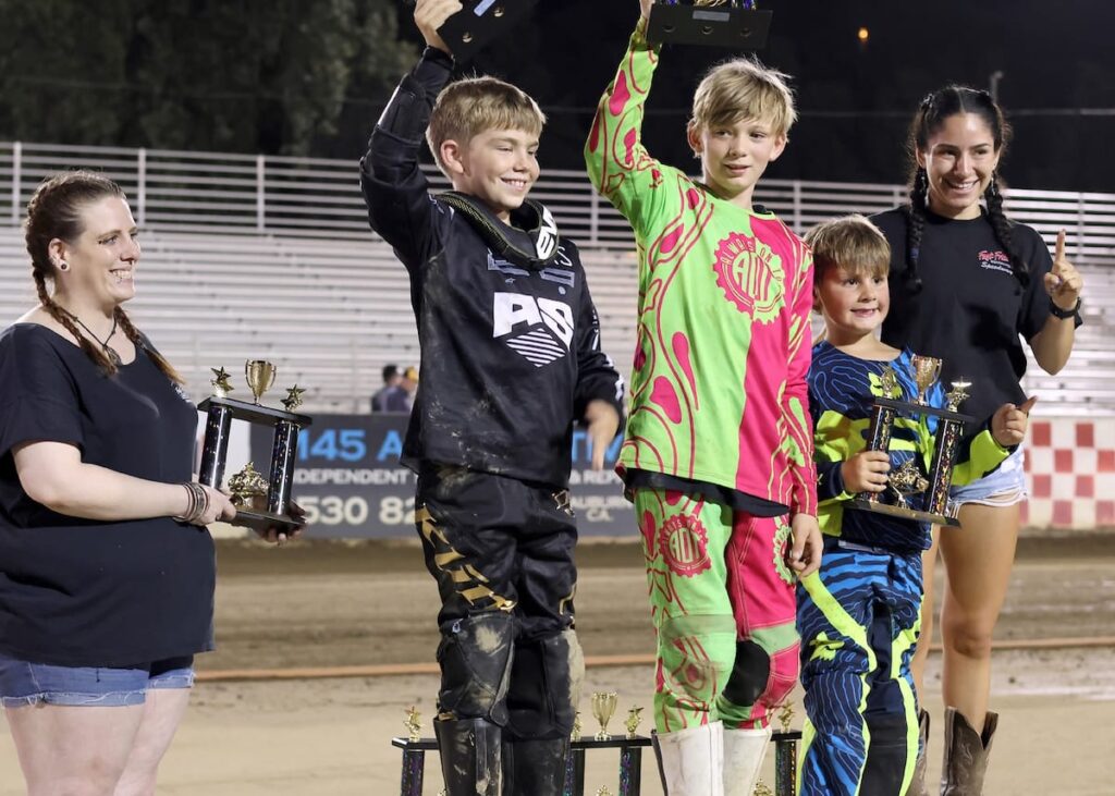 Youth 150cc divisions winners took to the podium to celebrate their wins. Pictured (L-R) trophy girl Tracey Upham, second division winner Mason Howell, first division winner Riley Rearick, third division winner Dexter Orlando and trophy girl Emma Schwartz. May 30 2025 - More great racing at Fast Friday’s Motorcycle Speedway in Auburn CA.