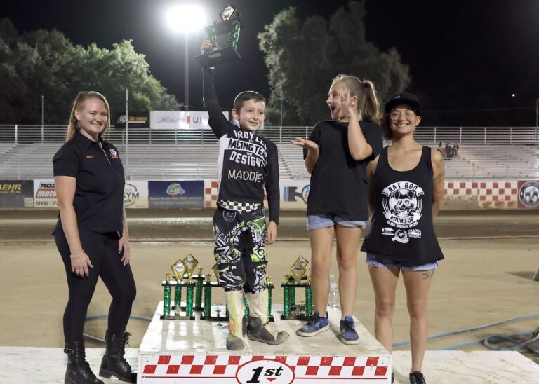 Ryder Faria (center) hold up his trophy high with a huge grin as Fast Fridays trophy girls (left-right) Kelly Craven, Faria, Lily Sneed and Leni Crow look on. Aug 8 2025 - Championship racing begins at Fast Friday’s Motorcycle Speedway in Auburn, CA.