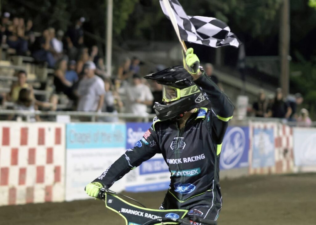 Brady Landon raises the checkered flag high after winning the scratch main event Friday night at Fast Friday's. Landon also was second in the handicap main event. July 10 2026 - 2026 Speedway & Team Challenge Round #4.
