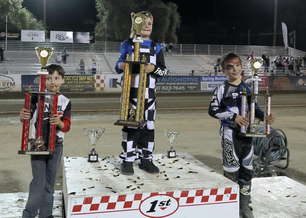 Holding trophies high are the Pee-Wee track champions. First-place finisher Dexter Orlando (center) second-place finisher Ricky Janniro (left) and third-place finisher Clyde Rivera (right). Sept 5 2026 - 2026 Fast Fridays Track & Pee Wee Championships.
